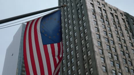 La-Bandera-Americana-Sopla-Orgullosamente-En-El-Viento-Con-Un-Gran-Edificio-Detrás