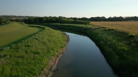 Aerial-above-narrow-creek-between-grassy-fields