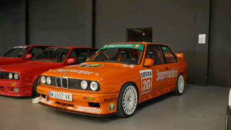 Full-shot-view-of-orange-sport-BMW-E30s-on-display-at-car-show,-indoor