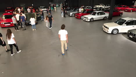 Aerial-view-following-fans-entering-and-admiring-BMW-e30-classic-cars-in-warehouse-car-show-event