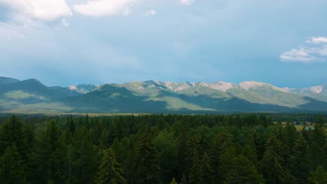 Luftdrohne-Fliegt-über-üppigen-Grünen-Wald-Von-Bäumen-Mit-Wolken,-Die-Schatten-über-Die-Bergkette-Von-Montana-Im-Hintergrund-Werfen