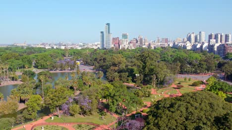 Dolly-in-aerial-view-of-the-Palermo-Rose-Garden-in-spring-with-characteristic-greenery-and-the-city-skyline-in-the-background,-Buenos-Aires,-Argentina