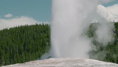 Old-Faithful-geyser-water-blasting-into-air-at-Yellowstone-national-park-natural-hot-springs,-zoom-out-hand-held-in-slow-motion