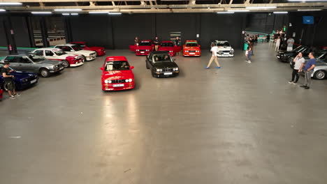 Classic-custom-BMW-e30-cars-parking-in-club-warehouse-car-show,-Slow-aerial-orbiting-view