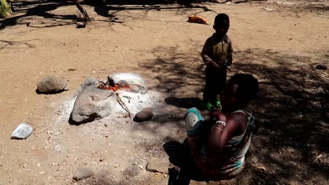 Hadzabe-tribe-mother-and-child-next-to-a-bonfire-ready-to-cook-on-the-ground-in-African-village