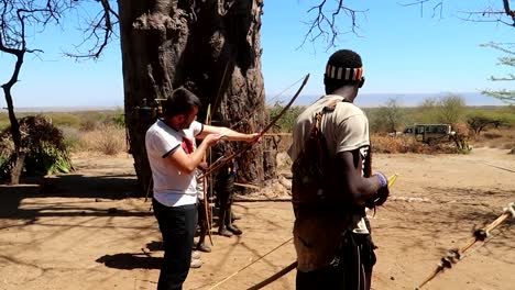 A-tourist-being-taught-how-to-use-a-bow-and-arrow-in-the-African-Desert-by-the-Hadzabe-Tribe