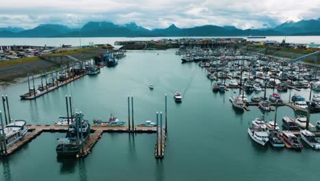 Aerial-drone-pull-away-of-halibut-Fishing-boats-pulling-into-marina-and-docking-in-small-town-Homer-Alaska-with-beautiful-mountain-range-backdrop