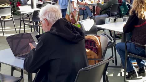 Tired-elderly-businessman-works-in-the-cascais-market-coffee-with-a-laptop-and-doing-a-call-using-his-phone