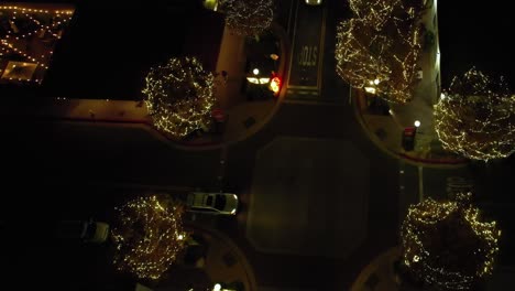 Trees-illuminated-with-Christmas-lights-on-quiet-crossroad-junction-at-night,-Aerial-Birdseye-view