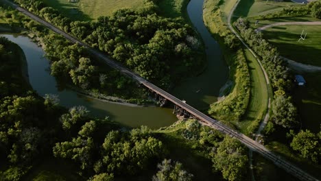 Aerial-view-rotating-around-gorgeous-snake-river-with-green-terrain-and-forest-with-railroad-track-across-the-river