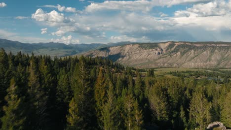 Aerial-drone-flying-through-tall-green-trees-and-rocky-hills-to-reveal-vast-Montana-mountain-range