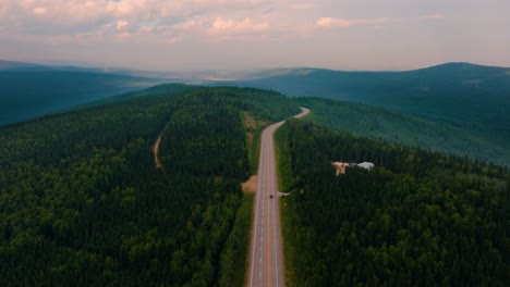 Aerial-drone-flyover-2-lane-highway-in-the-middle-of-nowhere-Montana-with-lush-green-trees-and-mountains-in-the-background-at-sunset