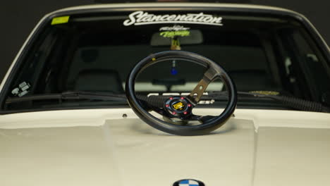 Sporty-steering-wheel-on-the-hood-of-stylish-white-BMW-e30-classic-sports-car-at-Barcelona-fan-meeting