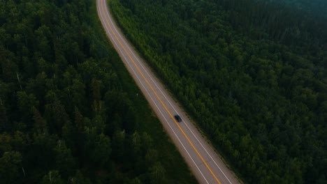 Aerial-drone-follow-of-lone-car-driving-on-two-lane-tree-lined-highway-in-the-middle-of-nowhere-Alaska