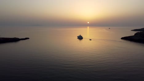 A-mesmerizing-aerial-shot-of-the-sea-in-Loutra,-Kythnos-during-sunrise,-following-a-yacht