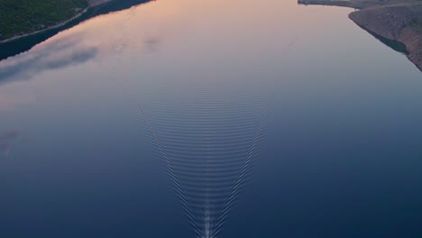 Boat-forming-v-shape-ripples-in-flat-calm-water-of-Adriatic-sea-at-sunrise,-aerial