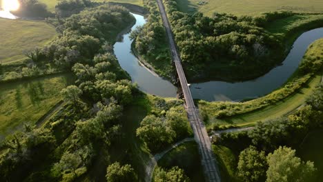 Aerial-|-Beautiful-river-surrounded-by-greenery-with-railroad-bridge-connecting-both-sides-of-land