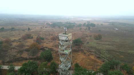 Aerial-footage-circling-a-watchtower-in-a-heather-nature-reserve,-on-a-cold-autumn-day