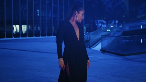 Mujer-Latina-Sexy-Caminando-En-La-Ciudad-Con-Un-Vestido-Negro-Con-Luces-Azules-En-El-Fondo