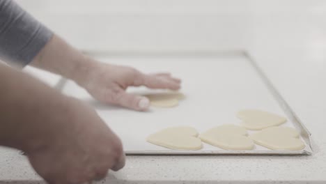 A-steady-shot-of-a-man-arranging-freshly-rolled-out-heart-shaped-butter-cookies-on-a-baking-tray-in-a-pastry-shop,-4K