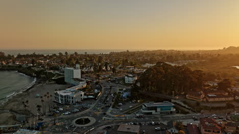 Santa-Cruz-California-Aerial-v10-fly-above-beach-street-leading-to-west-cliff-drive,-flyover-roundabout-at-wharf-entrance,-big-glowing-sun-setting-in-the-skyline---Shot-with-Mavic-3-Cine---May-2022