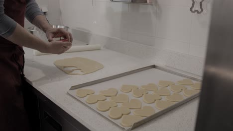 Cutting-out-a-heart-shaped-butter-cookie-and-putting-it-on-a-baking-tray-in-an-artisanal-pastry-shop