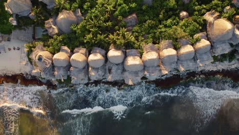 Top-down-aerial-view-of-Azulik-Hotel-in-Tulum,-México-during-sunset-near-a-beach-with-breaking-waves