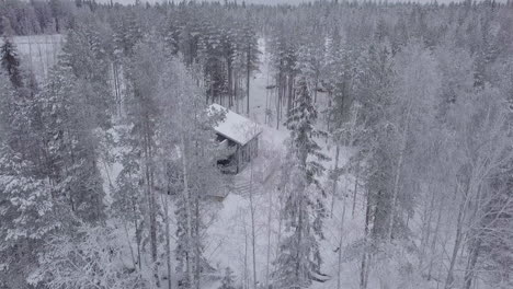 Aerial-View-Modern-Winter-Cabin-on-hill-in-snowy-Northern-forest,-Christmas-and-Ski-Vacation-Scene