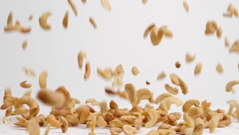 Salted,-roasted-cashew-nut-halves-and-pieces-bouncing-into-a-pile-on-white-table-top-in-slow-motion
