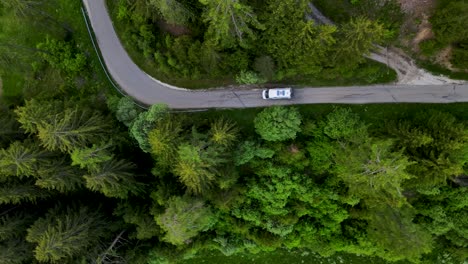 drone-flying-top-down-from-europe-forest-road-with-car-climbing-the-alps-aerial-footage