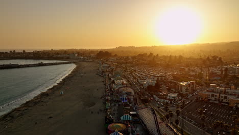 Santa-Cruz-California-Aerial-v9-cinematic-flyover-seaside-beach-boardwalk-amusement-park-along-the-street-with-beautiful-orange-glowing-sun-setting-in-the-sky---Shot-with-Mavic-3-Cine---May-2022