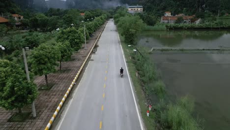 Cool-aerial-tilting-shot-following-bike-on-a-asian-road-sounded-my-water-and-stunning-green-mountains