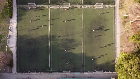 Luftaufnahmen-Von-Oben-Nach-Unten-Von-Spielern,-Die-Bei-Sonnenuntergang-Auf-Drei-Fußballfeldern-Fußball-Spielen,-Zeitraffer