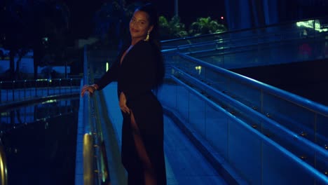 Sexy-hispanic-woman-spins-in-the-walkway-of-a-glass-building-wearing-a-black-dress-at-night