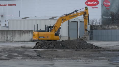 Side-View-Of-An-Excavator-Moving-Outside-Industrial-Building-In-Park-West-Business-Park,-Dublin,-Ireland