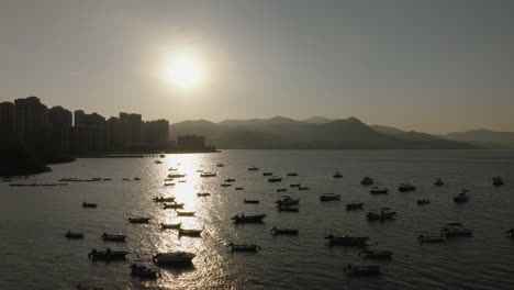 Drone-shot-of-bustling-port-with-silhouette-of-boats-at-dusk-in-Hong-Kong,-China