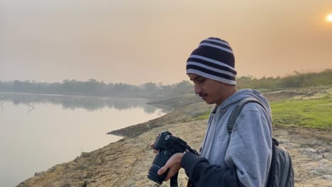 Closeup-portrait-of-young-man-taking-photographs-of-polluted-river,-hazy-morning
