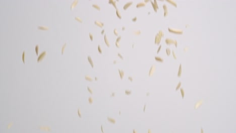Sliced,-blanched-almond-nut-pieces-raining-down-on-white-backdrop-in-slow-motion