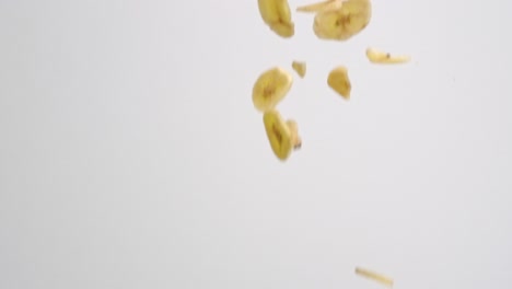 Freeze-dried-banana-slices-falling-on-white-backdrop-in-slow-motion