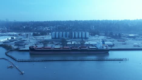 Ukrainian-freighter-docked-loading-wheat-grains-from-Canadian-port-Surrey-BC-aerial-drone-hold-overlooking-commercial-vehicles-working-with-staff-sunny-summer-day-clear-sky-silo-mylar-type-bags-cans