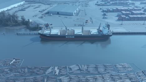 freighter-top-view-lumber-distribution-export-import-sunny-day-aerial-hold-nobody-quiet-on-break-between-loading-next-to-storage-containers-loading-bay-ship-has-cranes-on-vessel-calm-waters