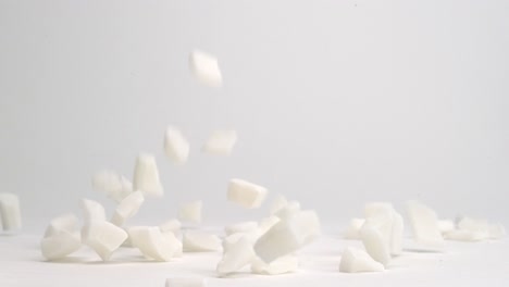 Cubed-white-coconut-chunks-falling-and-bouncing-onto-white-table-top-into-pile-in-slow-motion