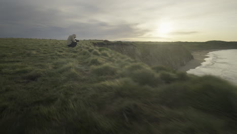 Female-landscape-photographer-squatting-at-Fortrose-cliff-edge-during-sunrise