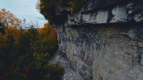 FPV-aerial-drone-view-flying-along-a-rock-wall-and-over-a-colorful-autumn-forest