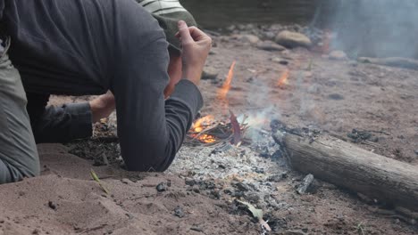 A-man-blows-on-a-fire-on-the-banks-of-a-river-bed-in-Victorias-high-country