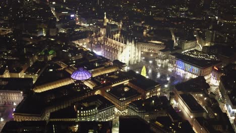 Milan-Cathedral-at-night-with-glowing-city-lights,-aerial-view