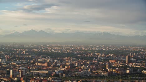 Milan-cityscape-during-golden-sunset-and-foggy-mountains-in-horizon,-view-from-above