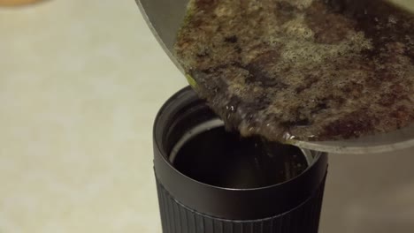 Pouring-liquid-green-brown-sludge-into-french-press-cup-to-make-home-made-butter
