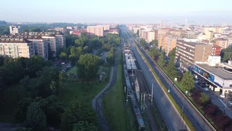 Subway-leaving-station-in-suburbs-of-Milan-city,-aerial-drone-view