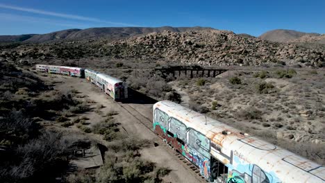 Verlassene-Eisenbahn-Mit-Mit-Graffiti-Bedeckten-Waggons-In-Der-Kalifornischen-Wüste